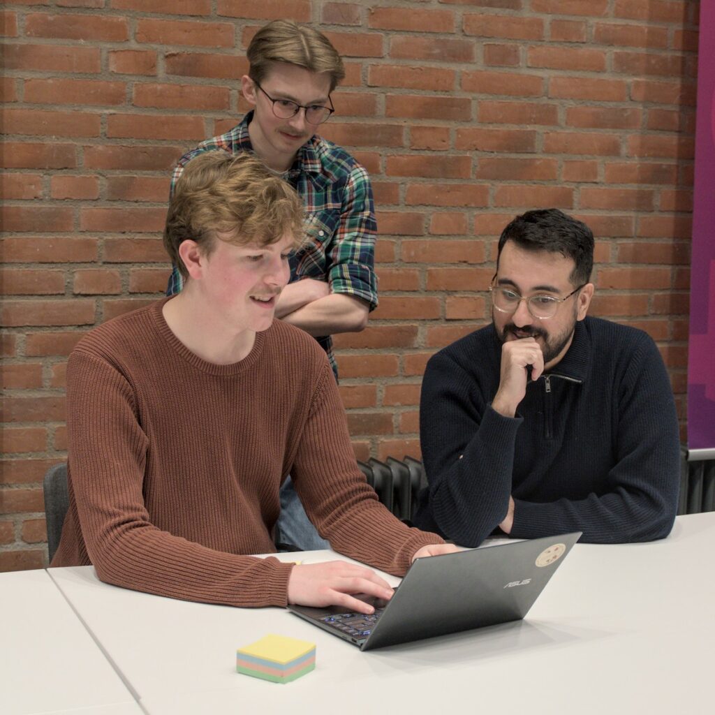 Tre studenter vid dator. Tittar på skärmen och diskuterar problem.
